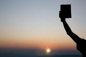 A man holding up a Bible against the rising sun.