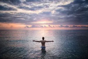 A man wading into the sea with arms outstretched.