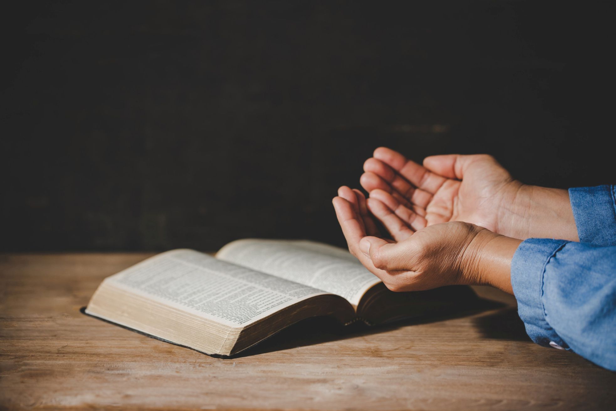 A person with arms cupped outward over an open Bible.