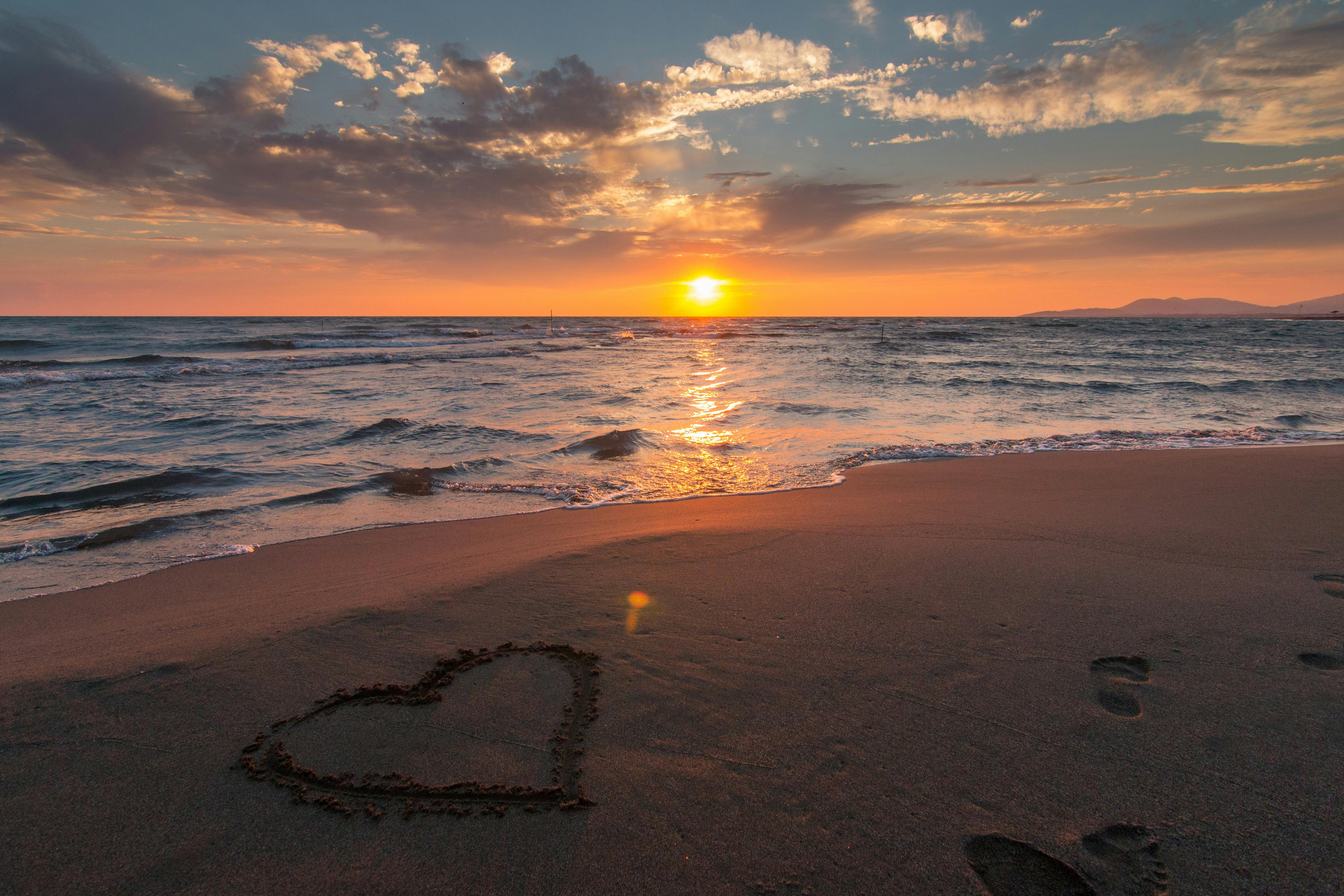beautiful sunset beach scene with heart shape drawn in sand beautiful sunset beach scene with heart shape drawn in sand